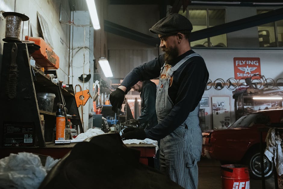Mechanic performing repairs in a vintage garage setting, using tools and machinery.