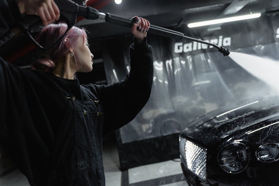 A young woman washing a car with a power spray in a dimly lit garage.