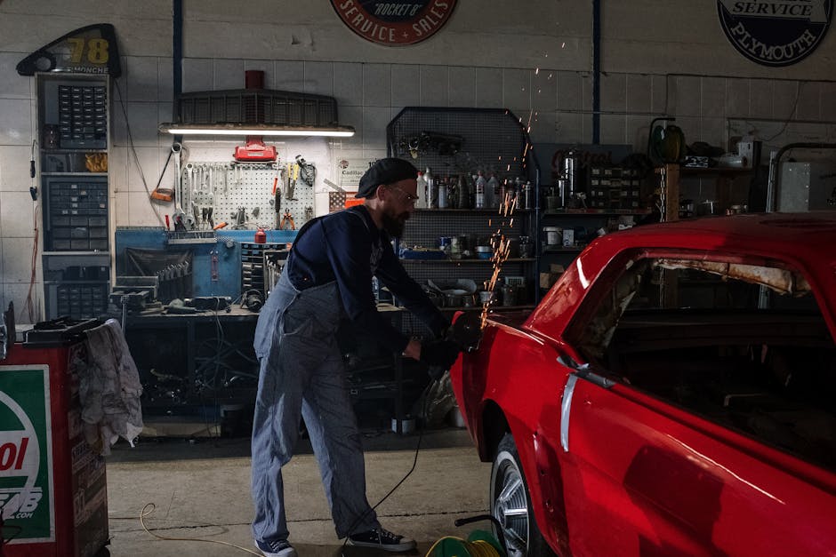 Mechanic restoring a vintage red car in a well-equipped garage with sparking grinder.